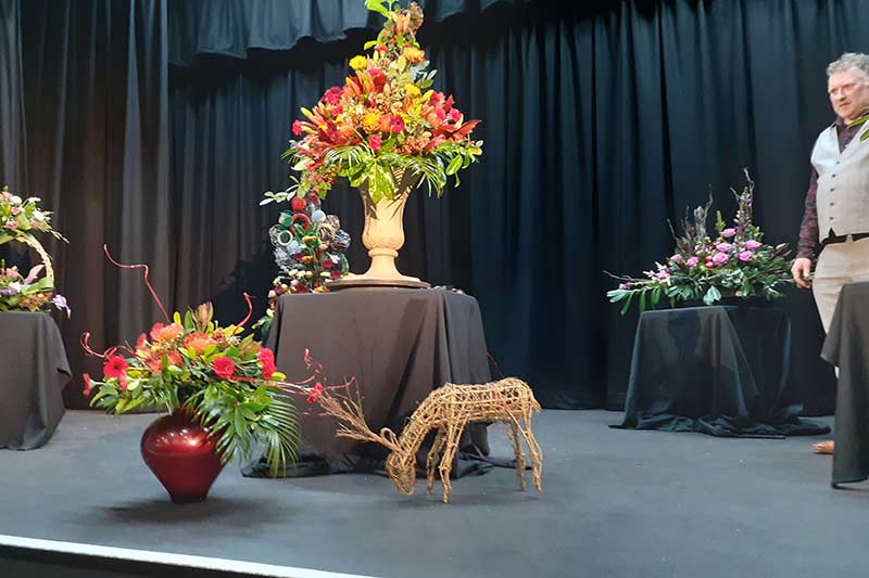 Donald Morgan on the stage with some of his arrangements at Ashton Hayes and Tarvin Flower Club's Christmas Meeting